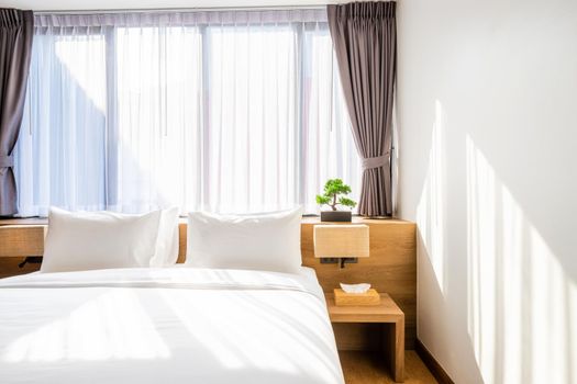 Close-up of white pillow on bed decoration with light lamp, tissue boxand and green tree in flowerpots in hotel bedroom interior.