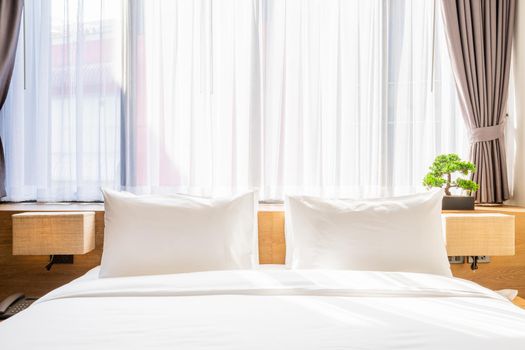 Close-up of white pillow on bed decoration with light lamp and green tree in flowerpots in hotel bedroom interior.