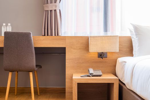 Close-up of white pillow on bed decoration with light lamp, chair and digital telephone set in hotel bedroom interior.
