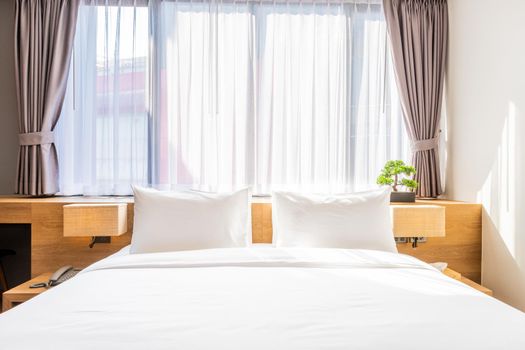 Close-up of white pillow on bed decoration with light lamp and green tree in flowerpots in hotel bedroom interior.