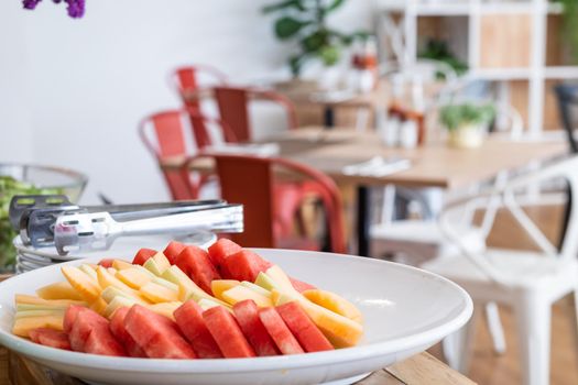 Chop the pieces of watermelon and pineapple in white dish the dining and flower vase on table decorationat buffet self service at hotel.