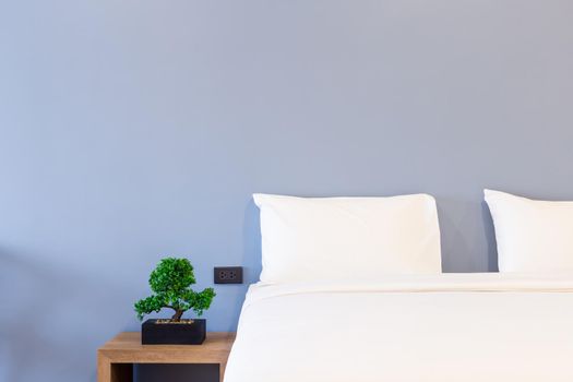 Close-up of white pillow on bed decoration with green tree in flowerpots in hotel bedroom interior.