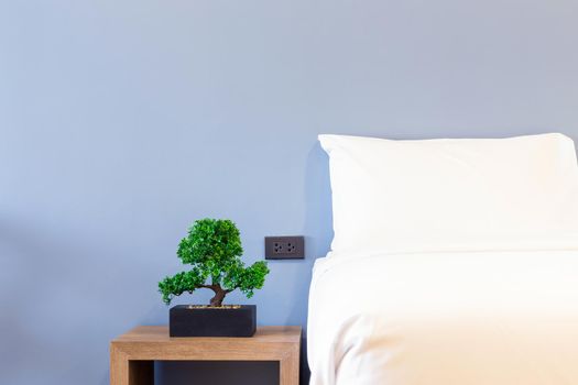 Close-up of white pillow on bed decoration with green tree in flowerpots in hotel bedroom interior.