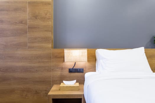 Close-up of white pillow on bed decoration with light lamp and tissue box in hotel bedroom interior.