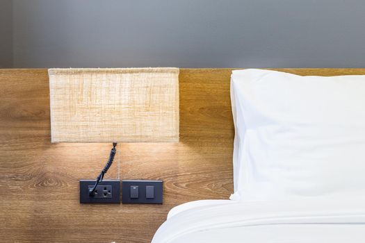 Close-up of white pillow on bed decoration with light lamp in hotel bedroom interior.