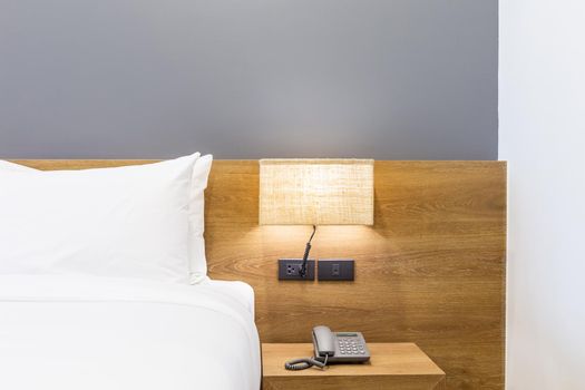 Close-up of white pillow on bed decoration with light lamp and digital telephone set in hotel bedroom interior.