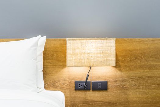 Close-up of white pillow on bed decoration with light lamp in hotel bedroom interior.