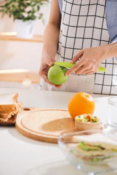 Hands of a woman is making school lunch box in the red color. It is more interesting for children. Caucasian female preparing food (fruits and vegetables) for healthy eating child (kid).