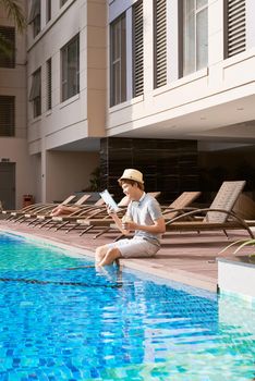 Young asian man reading book by the pool on a sunny summer day