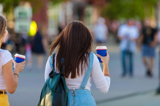 Two girlfriends of the girl are walking down the street and drinking from a glass of coffee.