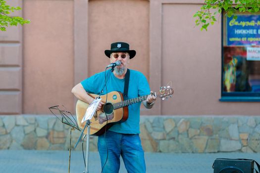 An adult gray-haired man plays guitar and sings on a city street. Street musician.