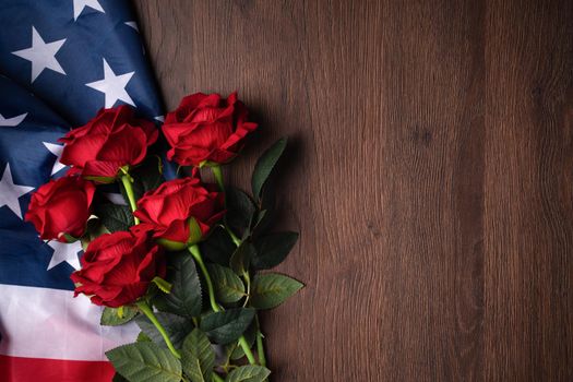 Concept of U.S. Independence day or Memorial day. National flag and red rose over dark wooden table background.