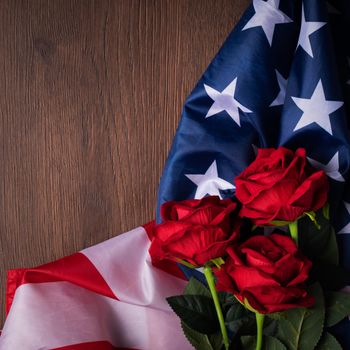 Concept of U.S. Independence day or Memorial day. National flag and red rose over dark wooden table background.