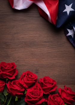 Concept of U.S. Independence day or Memorial day. National flag and red rose over dark wooden table background.