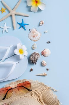 Summer beach background design concept. Top view of holiday travel with shells, hat, slipper on blue background.