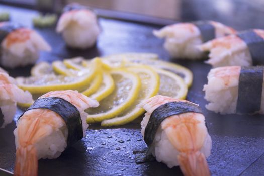 Assorted sushi food on a black slate plate. No people