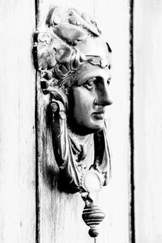 Vintage door knocker face shape on brown wooden door in Altea, Alicante, Spain