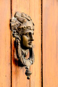 Vintage door knocker face shape on brown wooden door in Altea, Alicante, Spain