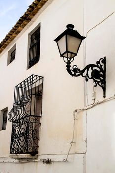 Whitewashed facade with window with forged metal grill and vintage streetlight in Altea village, Alicante, Spain