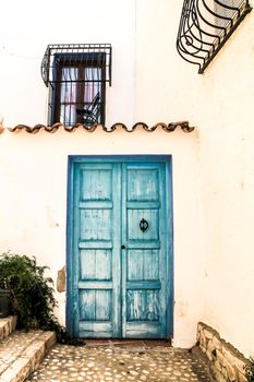 Whitewashed facade with colorful blue wooden door and windows with forged metal grill in Altea, Alicante, Spain