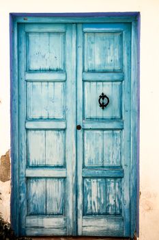 Blue wooden door with black metal knocker and whitewashed facade in Altea, Alicante, Spain.