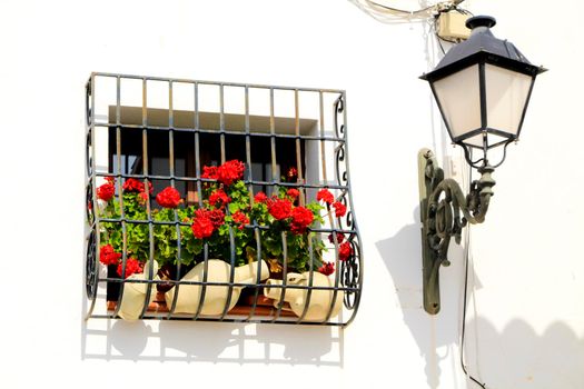 Beautiful whitewashed facade with colorful geranium plant in the window and  vintage streetlight in Altea village, Alicante, Spain