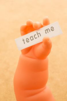 Toy doll hand holding paper with TEACH ME wording