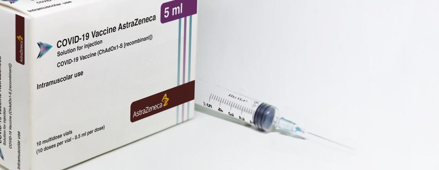 Cambridge, UK, february 5th 2021: A syringe next to the AstraZeneca Covid-19 Vaxzevria vaccine box isolated on a white background. Health and prevention. Copy space and banner. Selective focus