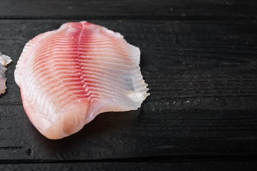 Raw white fish fillet cuts, on black wooden background with copy space for text