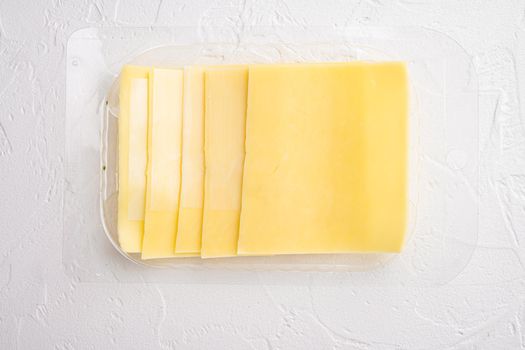 Pieces of Cheddar cheese set, in plastic pack, on white stone background, top view flat lay