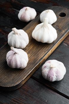 Pile of organic farm garlic set, on wooden cutting board, on old dark wooden table background