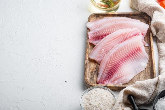 Raw white fish tilapia, with basmati rice and cherry tomatoes ingredients, on white background, top view with copy space for text