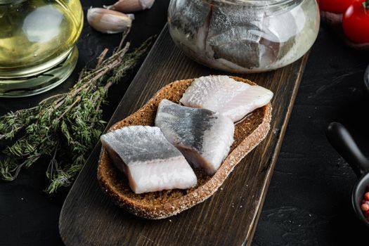 Atlantic wild herring, Pickled Canned fish preserves set, on wooden cutting board, on black background with herbs and ingredients