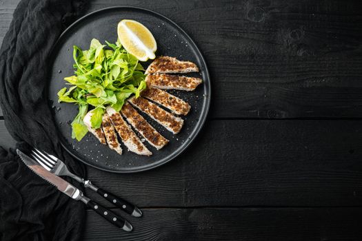 Crumbed, chicken breast fillet grilled, over black wooden table, top view with space for text