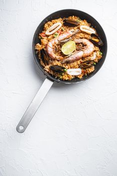 Paella cooked in frying pan on white textured background, flat lay with copy space, food photo.