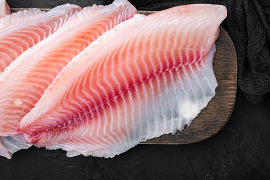 Raw white fish fillet cuts, on black background, top view