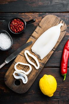 Raw squid, sliced for rings on cutting board with lemon and pepper over dark rustic wooden background, flat lay, food photo.