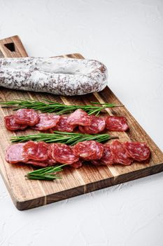 Fuet whole and sliced cuts, spanish dry cured sausage on white surface.