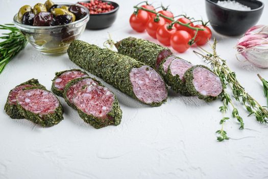 Traditianal fuet sausage in herbs with ingredients on white textured background.