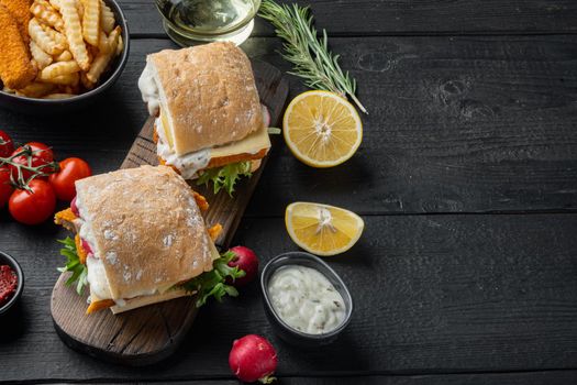 Fish fingers sandwich set, on wooden cutting board, on black wooden table background , with copyspace and space for text