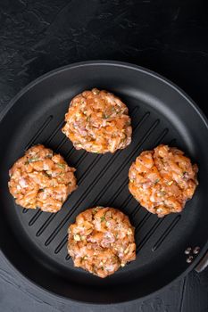 Raw fish patties with salmon fillet and lemongrass, on black textured background, flat lay