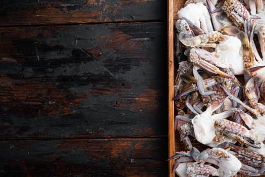 Frozen raw blue swimming crab claws set, in wooden box, on dark wooden background, top view flat lay , with copyspace and space for text