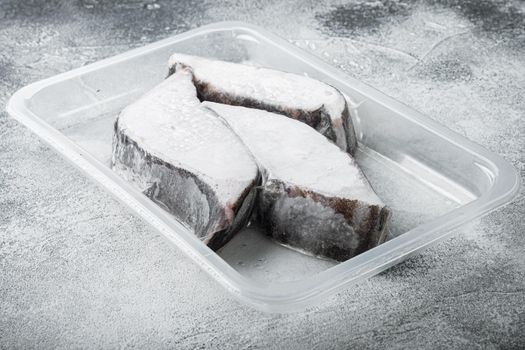 Frozen Greenland halibut steaks vacuum pack set, on gray stone table background, with copy space for text