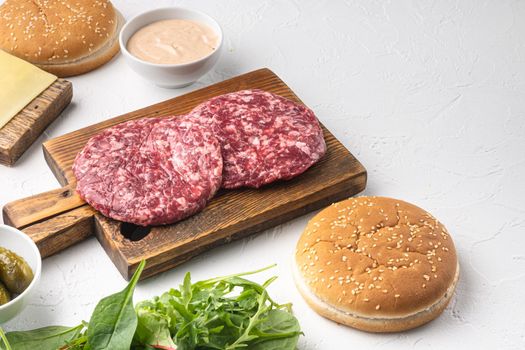 Homemade hamburger. Raw beef patties, sesame buns with other ingredients set, on white stone background, with copy space for text
