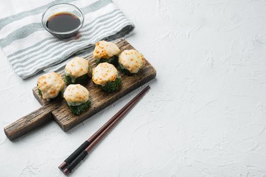 Baked sushi maki rolls with salmon, crab, cucumber, avocado, flying fish roe and spicy sauce set, on white stone background , with copyspace and space for text