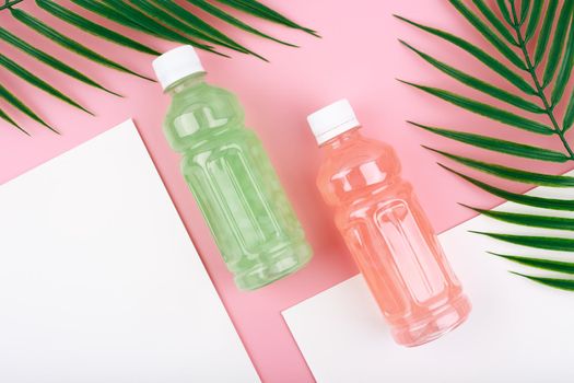 Creative flat lay with two transparent plastic bottles of pink and green detox drinks or fresh and healthy lemonades on pink and white background with palm leaves. Concept of healthy organic detox drinks for weight loss 