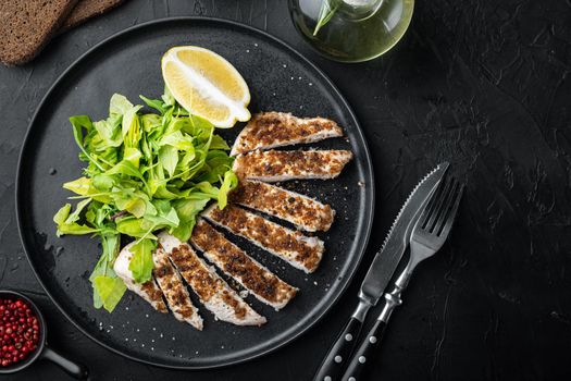 Crumbed, chicken breast fillet grilled, on black background, flat lay with copy space