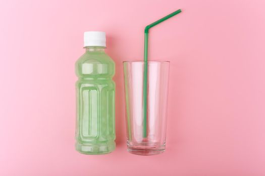 Creative flat lay with transparent plastic bottle with light green detox drink next to empty glass with green straw on bright pink background. Concept of weight loss, dieting and clean eating