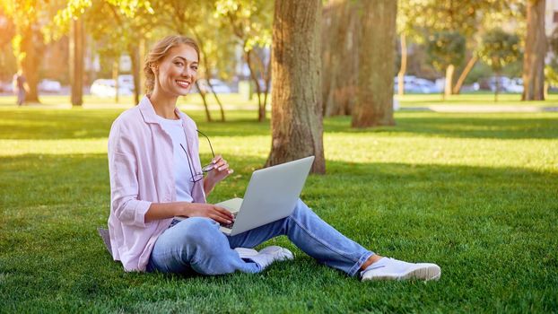Businesswoman sitting grass summer park using laptop Business person working remote. Outdoor Successful european caucasian woman freelancer make video call teacher study work online lessons