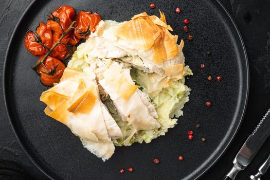 Freshly cooked Chicken Kiev oozing garlic and parsley butter set, with baked cherry tomatoes, mashed potatoes, on black stone background, top view flat lay
